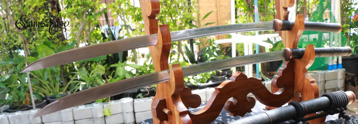 Two slim curved blades on the stand, with the scabbard below