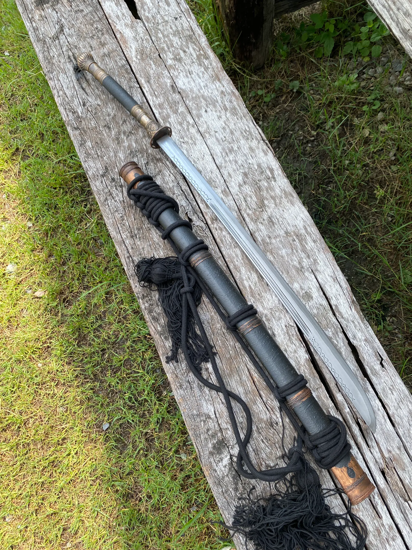 Laos Dhaab drawn beside its black textured-silk scabbard on a weathered plank