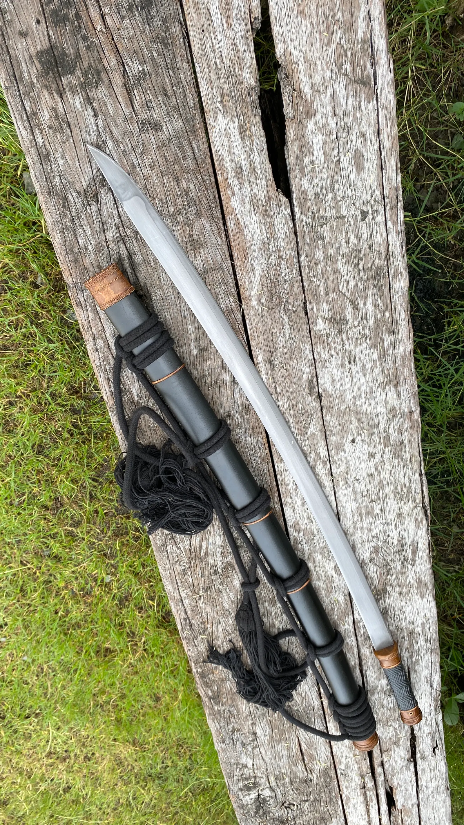The Thai Saber beside its black scabbard with copper bands, black rope coiled.