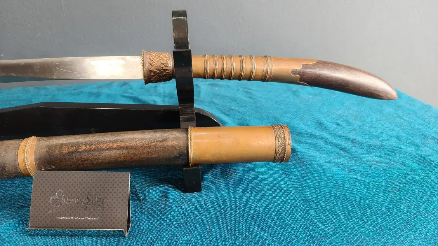 Hilt close-up: copper collar, ringed grip, curved pestle and the scabbard's copper mouth sleeve.