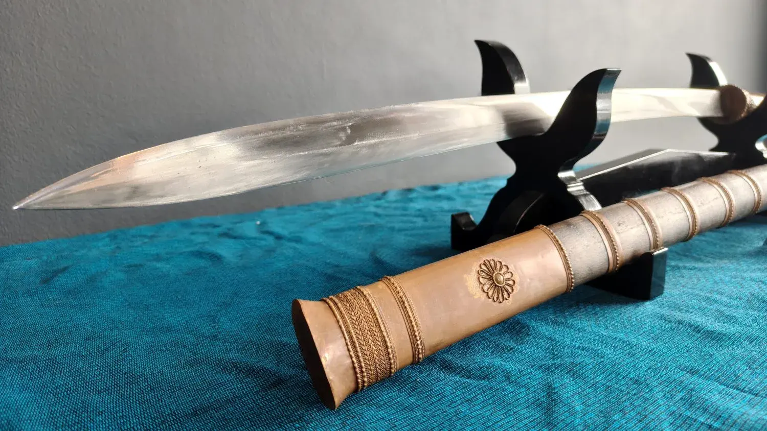 Blade point close-up, with the scabbard's filigree rosette sleeve and braided-wire bands.