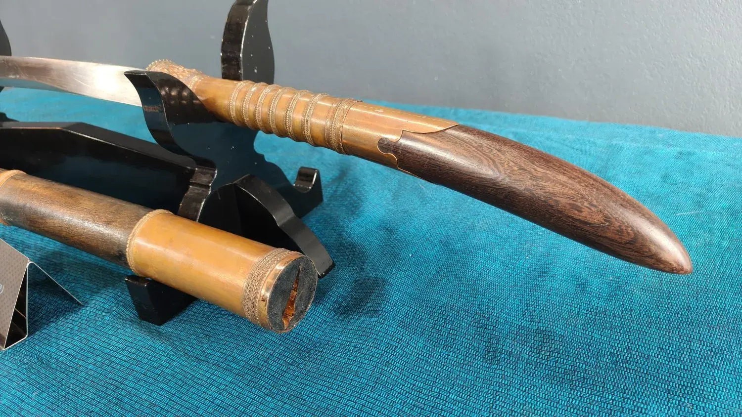The hilt from behind: ringed copper grip and dark-wood pestle; the scabbard toe.