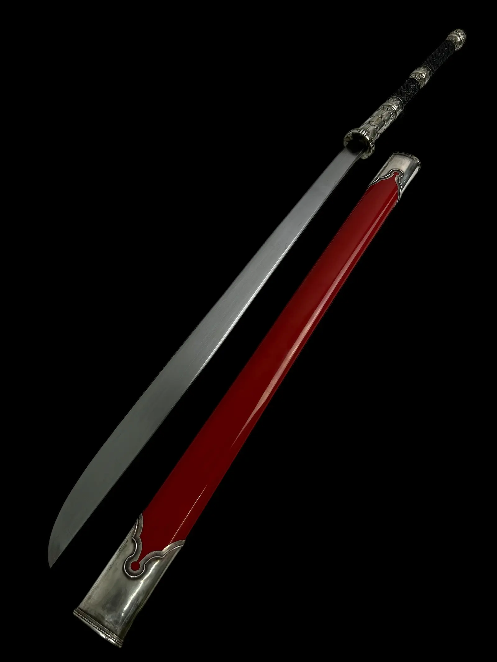 A crimson-lacquer scabbard with silver ends beside a drawn blade, on black.